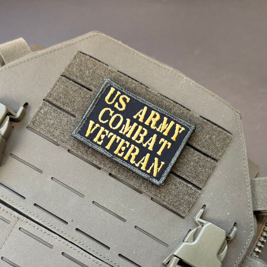 A rectangular embroidered patch reading 'US ARMY COMBAT VETERAN' in yellow lettering on a dark navy background, attached to a tan tactical vest with MOLLE webbing.