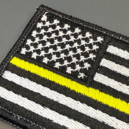 Thin Yellow Line American Flag embroidered morale patch: featuring a black-and-white American flag design with a single bright yellow stripe running horizontally, on a dark gray background.