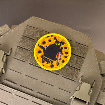 Murder Cat and Sunflowers printed canvas morale patch featuring a black cat holding a red knife on a yellow spotted background with the design lettering below it, attached to a tan tactical vest with Velcro and quick-release.