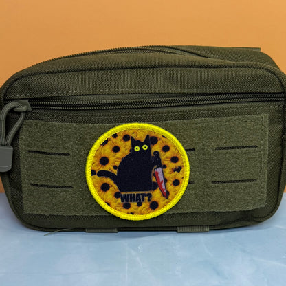 Murder Cat and Sunflowers printed canvas morale patch, an olive green tactical pouch with a hook-and-loop front panel, featuring a circular printed patch of a black cat holding a knife on a yellow spotted background with the.