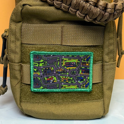 An olive drab tactical pouch with a green embroidered border patch featuring a colorful map design, shown against a solid orange background.