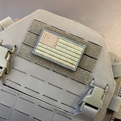 Subdued FDE Tactical American Flag embroidered morale patch: tactical patch featuring an American flag design in muted olive green, tan, and gray, mounted on a gray Velcro strip over a gray tactical vest or plate carrier.