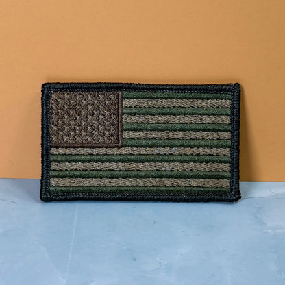 Subdued FDE Tactical American Flag embroidered morale patch: American flag patch in olive green, tan, and black, displayed on a light blue surface against a solid orange background.