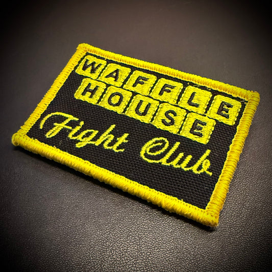 A rectangular embroidered patch with a black background and bright yellow border, featuring the words 'WAFFLE HOUSE Fight Club' in yellow lettering, photographed on a dark textured surface.