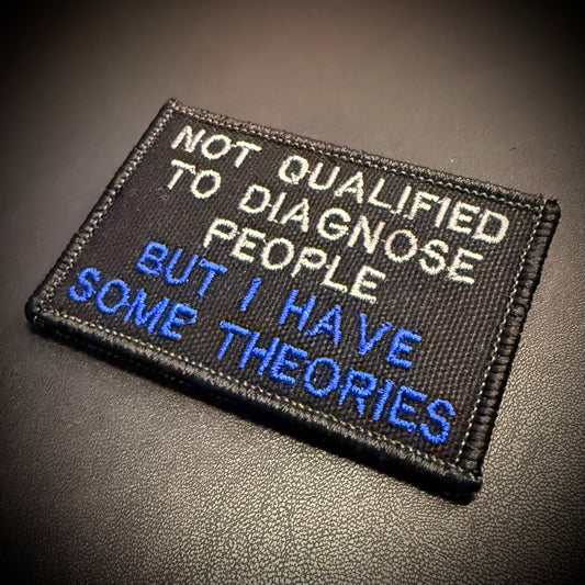A rectangular embroidered patch with black background and white and blue text reading 'NOT QUALIFIED TO DIAGNOSE PEOPLE BUT I HAVE SOME THEORIES,' photographed on a dark textured surface.