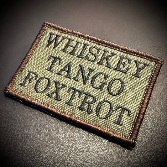 Whiskey Tango Foxtrot WTF embroidered morale patch: rectangular patch with the text 'WHISKEY TANGO FOXTROT' in black on an olive drab background, set against a dark background.