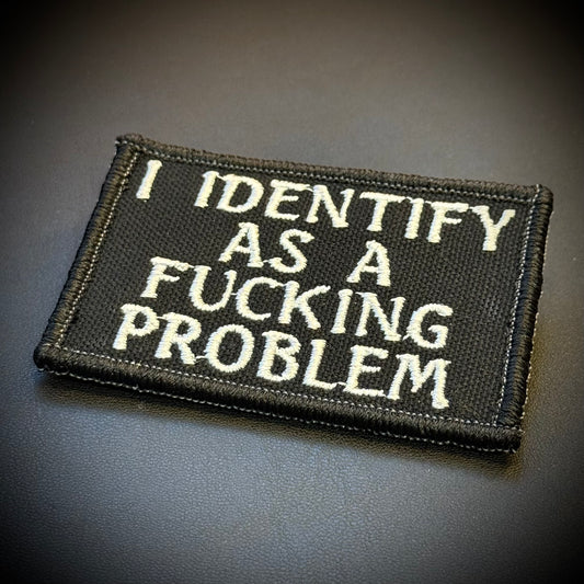 A rectangular black embroidered patch with white text reading 'I IDENTIFY AS A FUCKING PROBLEM' on a dark gray background.