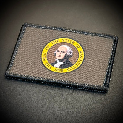 A rectangular tactical patch featuring the seal of the State of Washington, displayed on a dark textured surface.
