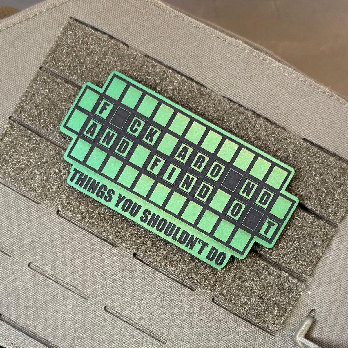 FAFO Game Show laser-engraved synthetic patch: a green and black laser-engraved synthetic patch with the text 'F*CK AROUND AND FIND OUT THINGS YOU SHOULDN'T DO' applied to a tactical gear strap.