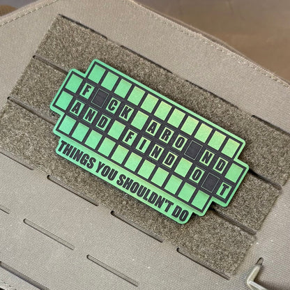 FAFO Game Show laser-engraved synthetic patch: a green and black laser-engraved synthetic patch with the text 'F*CK AROUND AND FIND OUT THINGS YOU SHOULDN'T DO' applied to a tactical gear strap.