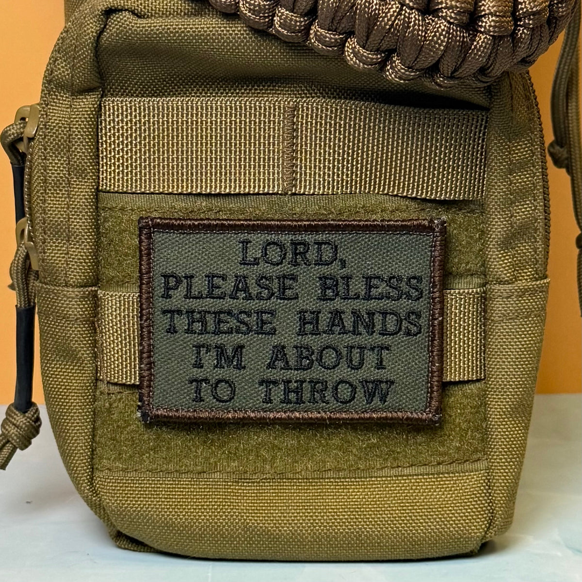 Lord, Bless These Hands I'm About To Throw embroidered morale patch: olive green tactical pouch with a sewn-on rectangular patch that reads, 'LORD, PLEASE BLESS THESE HANDS I'M ABOUT TO THROW.' A braided brown.