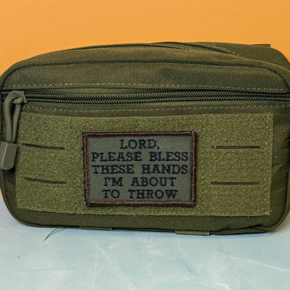 Lord, Bless These Hands I'm About To Throw embroidered morale patch: olive green tactical pouch with a front hook-and-loop patch that reads, 'LORD, PLEASE BLESS THESE HANDS I'M ABOUT TO THROW,' shown against an orange.