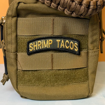 Army Regular Forces Funny Morale Patch Tab embroidered morale patch: olive drab tactical pouch with MOLLE webbing and a black embroidered patch reading 'SHRIMP TACOS' in gold lettering, shown against a solid orange background.
