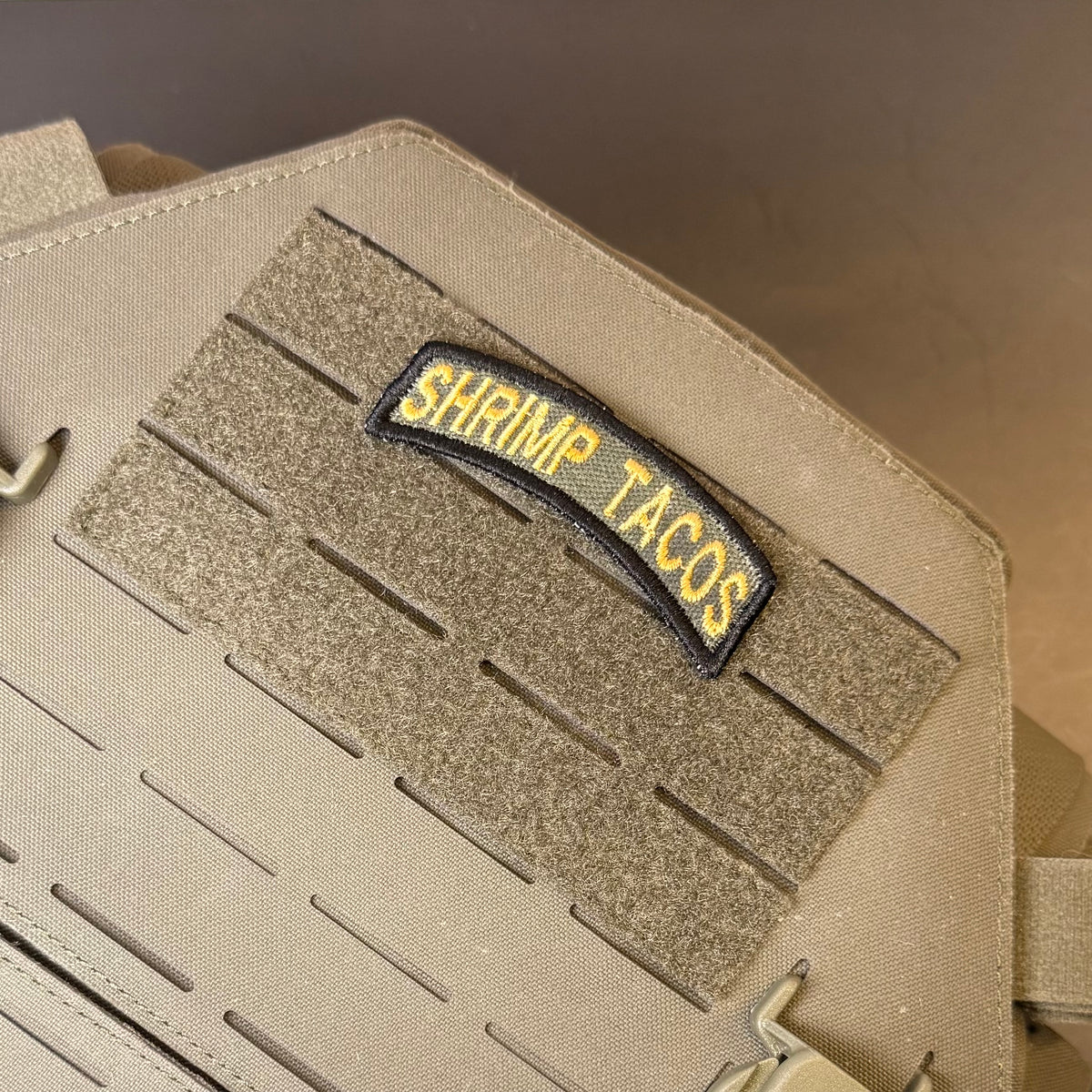 Army Regular Forces Funny Morale Patch Tab embroidered morale patch: tan tactical bag with a hook-and-loop panel and a black embroidered patch reading 'SHRIMP TACOS' in yellow.
