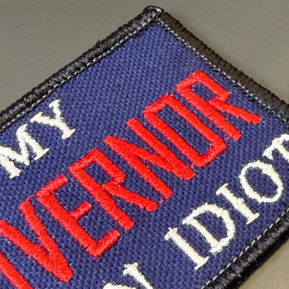 My Governor Is An Idiot embroidered morale patch: embroidered rectangular patch with a dark blue background, black stitched border, red embroidered text reading 'GUBERNOR', and white embroidered text partially visible.