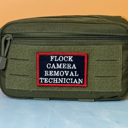 Flock Camera Removal Technician embroidered morale patch: olive green tactical pouch with a front zipper and a rectangular embroidered patch reading 'FLOCK CAMERA REMOVAL TECHNICIAN' in white on a dark navy background with a red.