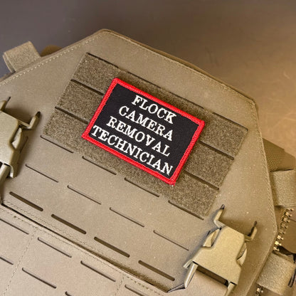 Flock Camera Removal Technician embroidered morale patch: with a black background, red border, and white text reading 'FLOCK CAMERA REMOVAL TECHNICIAN,' attached to a tan tactical vest or bag with hook-and-loop.