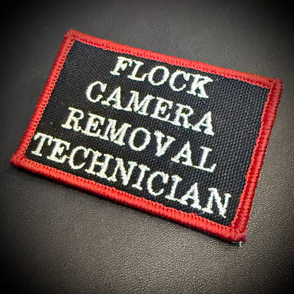 A rectangular embroidered patch with a black background, red border, and white text reading 'FLOCK CAMERA REMOVAL TECHNICIAN', shown on a dark textured surface.