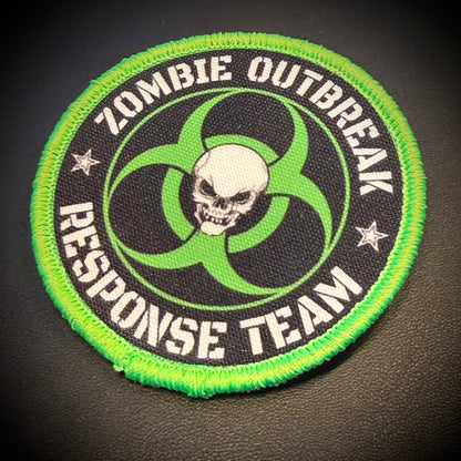 A circular embroidered patch with a bright green border, black center, white text reading 'ZOMBIE OUTBREAK RESPONSE TEAM,' a green biohazard symbol, and a white skull in the middle, shown on a dark textured background.