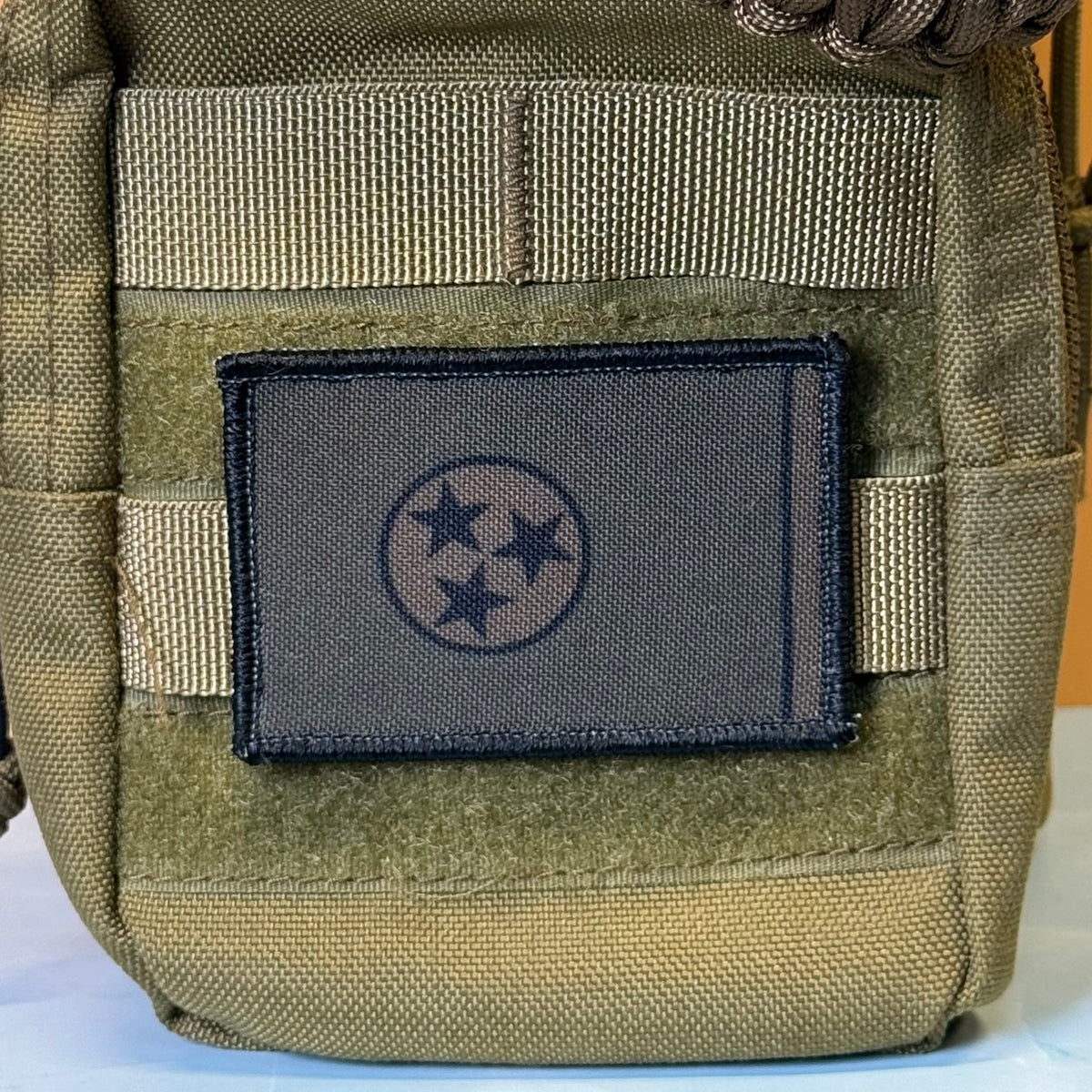 Tennessee State Flag printed canvas morale patch, close-up of a tactical pouch with a dark gray rectangular patch featuring the Tennessee state flag emblem, mounted on tan webbing.