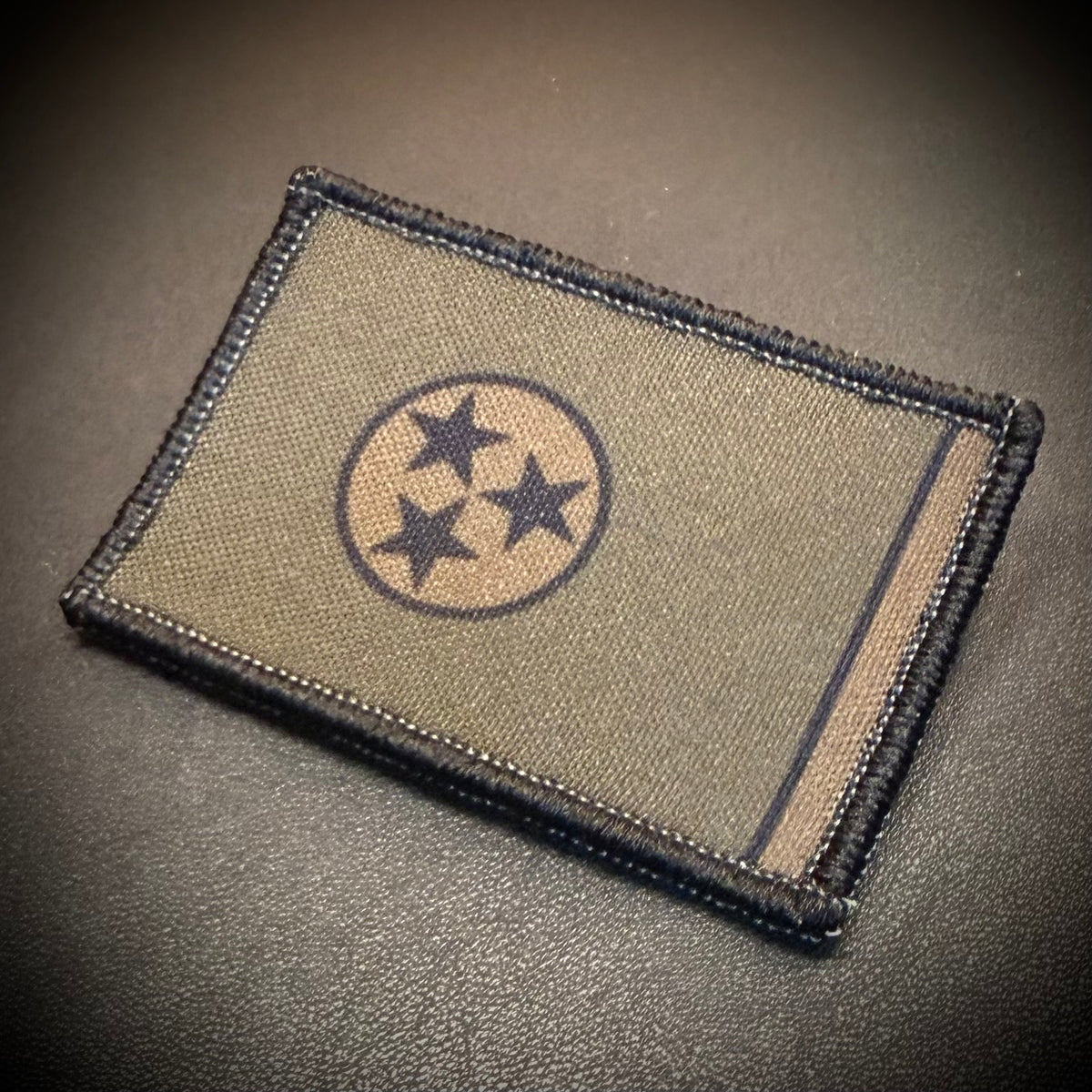 A rectangular embroidered patch featuring the Tennessee state flag design, including a circle of three stars, shown on a dark textured surface.