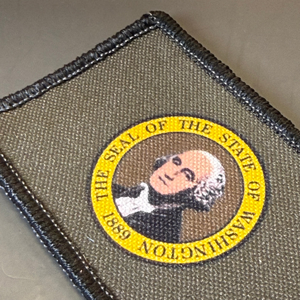 Washington State Flag printed canvas morale patch featuring the seal of the State of Washington, with a yellow circular border and a portrait of George Washington on an olive drab background.