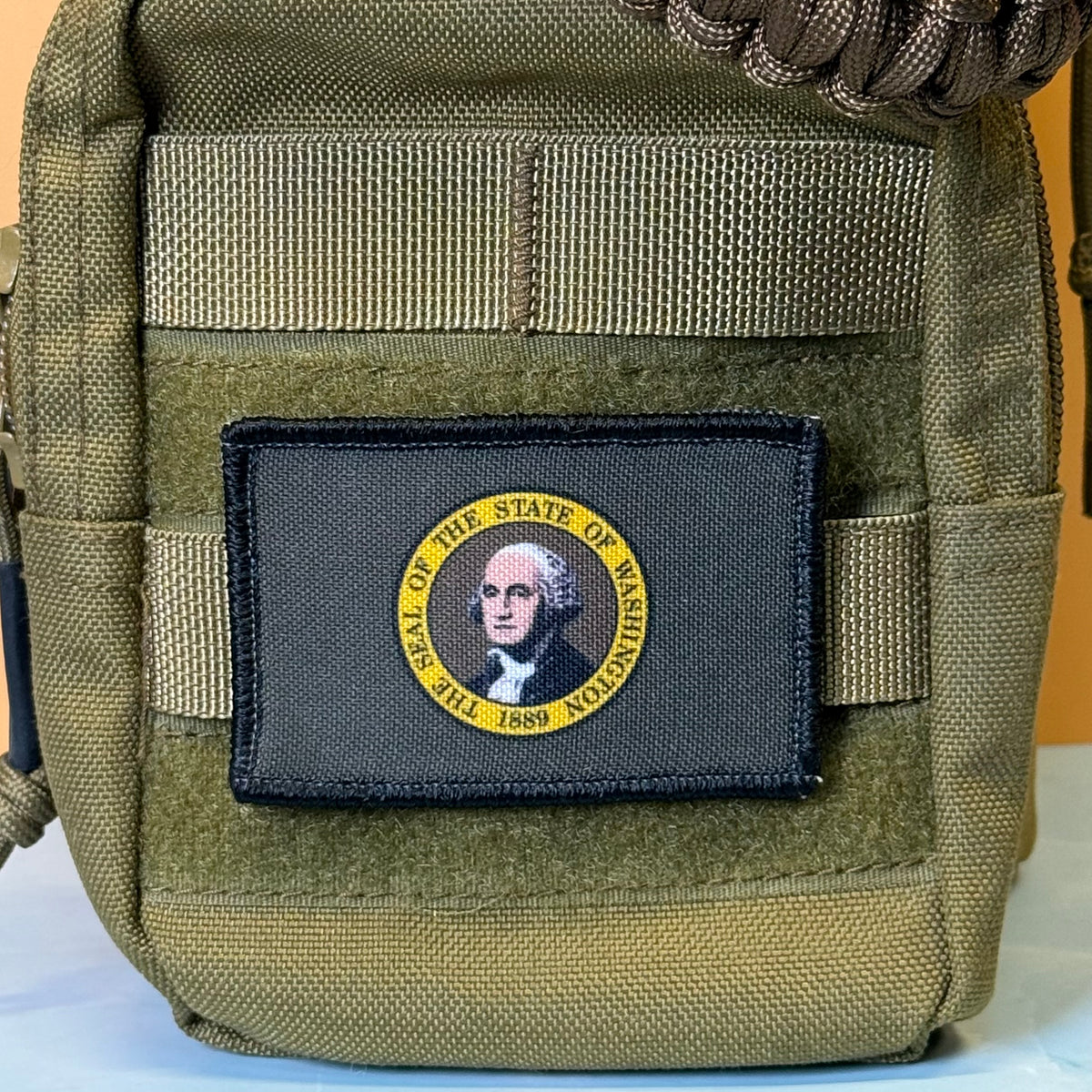 Washington State Flag printed canvas morale patch, an olive drab tactical pouch featuring a rectangular black patch with a yellow circular border and a portrait of George Washington, labeled 'SEAL OF THE STATE OF WASHINGTON 1789'.