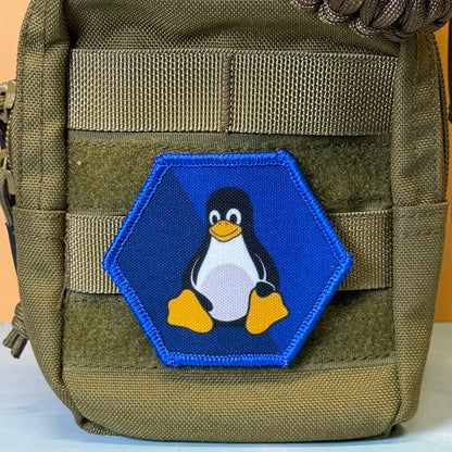 Linux Tux Penguin printed canvas morale patch, a close-up of an olive green tactical pouch featuring a hexagonal printed patch with the Tuxedo Linux penguin logo on a blue background.