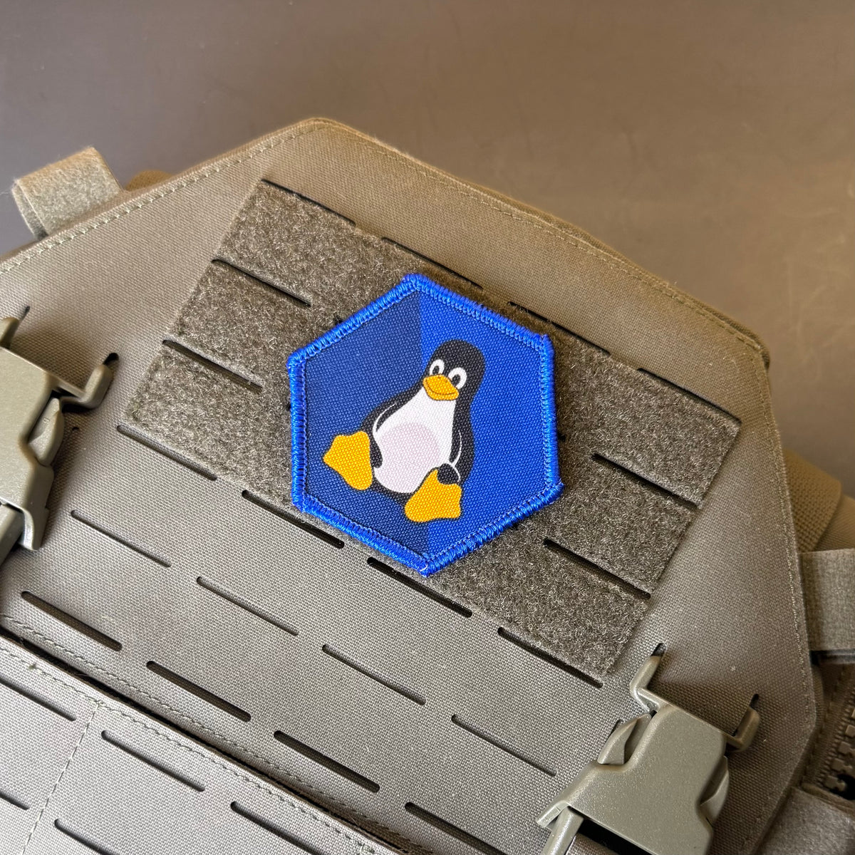 Linux Tux Penguin printed canvas morale patch featuring the Linux Tux penguin, attached to a tan tactical vest with MOLLE webbing.
