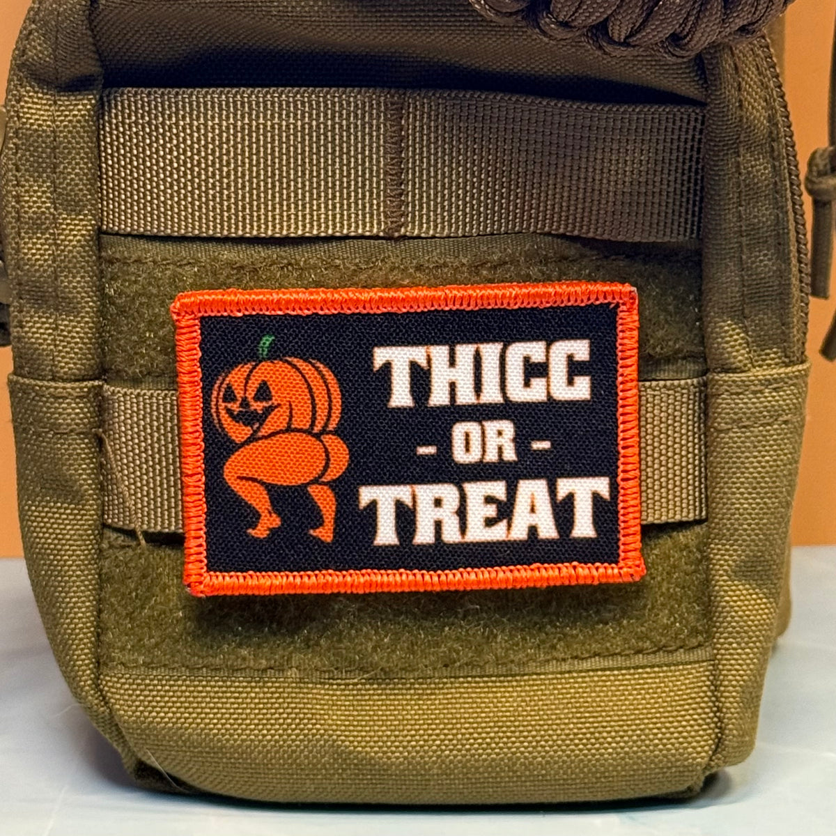 Thicc or Treat printed Halloween pumpkin morale patch attached to an olive green tactical pouch.