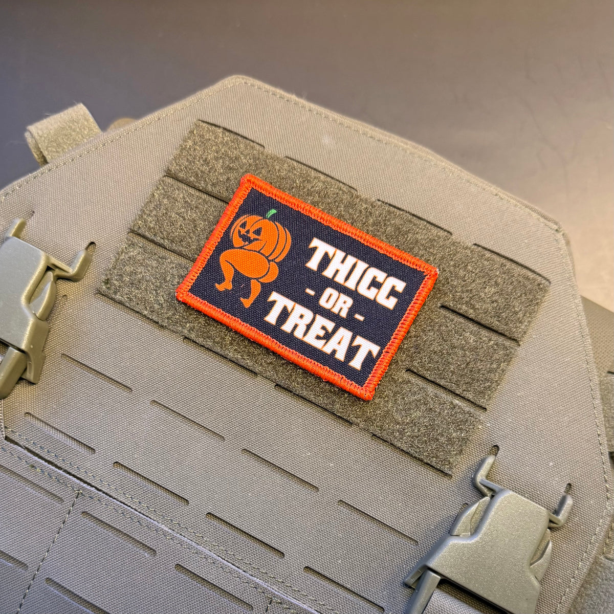 Thicc or Treat Halloween pumpkin printed morale patch attached to tan MOLLE webbing on tactical gear.