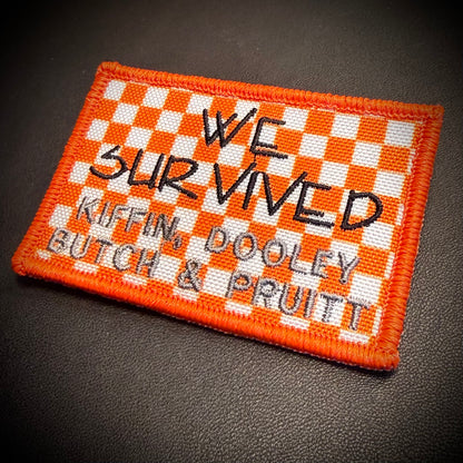An embroidered rectangular patch with an orange and white checkered border and background, featuring black text that reads 'WE SURVIVED KIFFIN, DOOLEY BUTCH & PRUITT' on a dark textured surface.