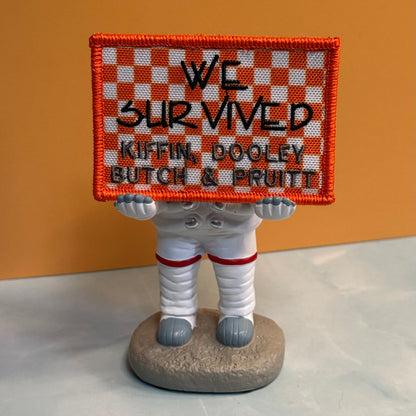 We Survived, Tennessee Football embroidered morale patch: small astronaut figurine holding a square embroidered sign that reads “WE SURVIVED KIFFIN, DOOLEY, BUTCH & PRUITT.” The sign has an orange and white checkered border.