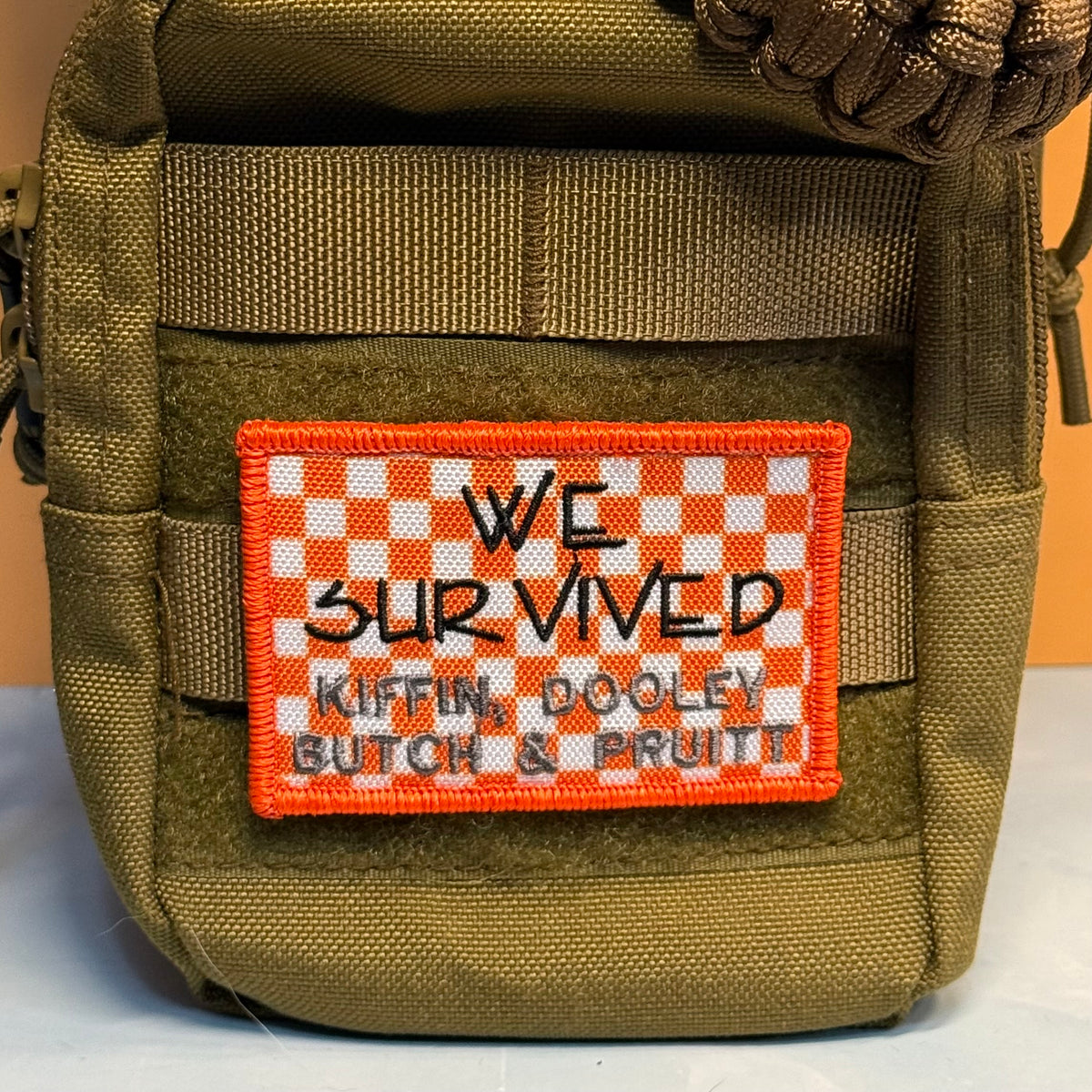 We Survived, Tennessee Football embroidered morale patch: olive drab tactical pouch featuring a rectangular embroidered patch with an orange and white checkered border and the text 'WE SURVIVED KIFFIN, DOOLEY BUTCH & BRUITT' in.