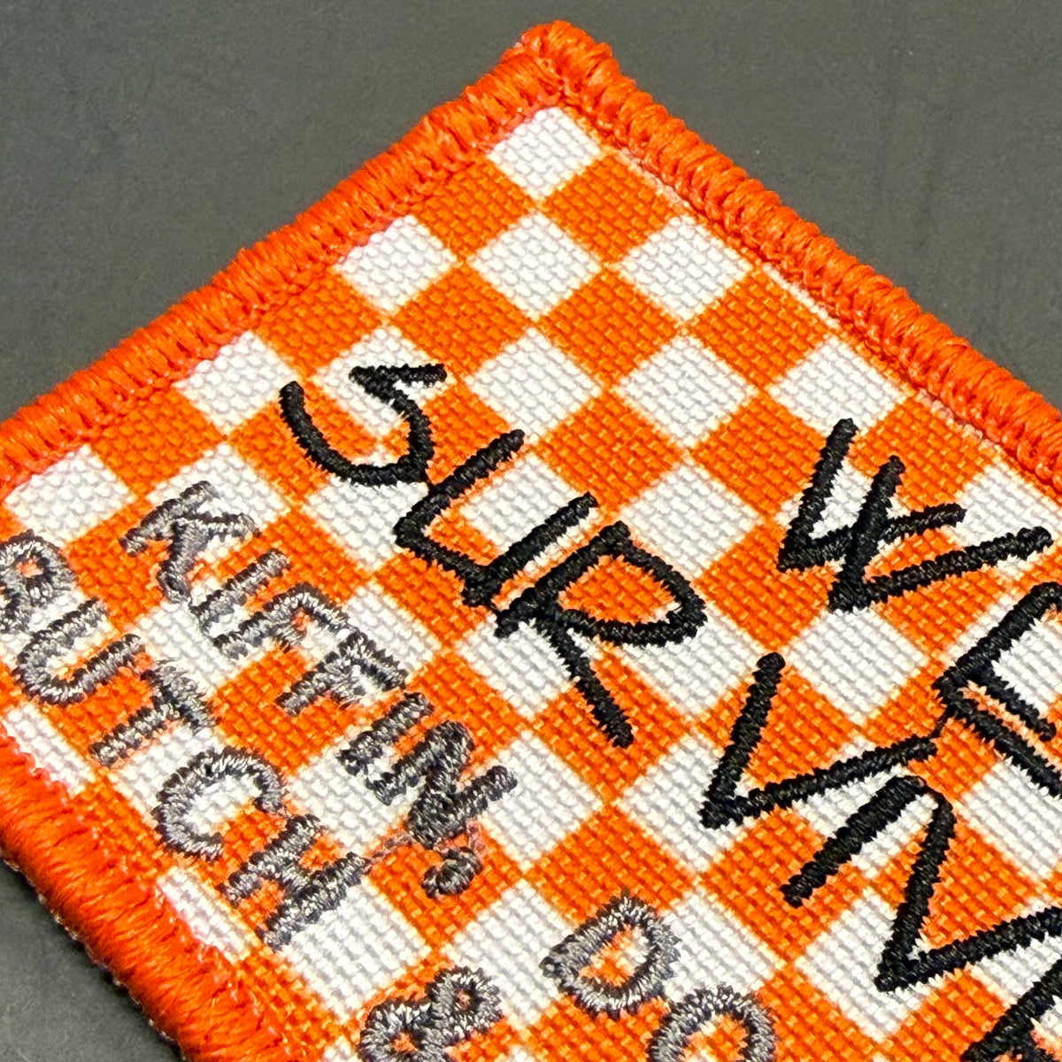 We Survived, Tennessee Football embroidered morale patch: embroidered square patch with an orange and white checkerboard pattern, black stitched text reading 'SURVIVE', and gray text reading 'KUFFIN'S CAUTCH & DO.