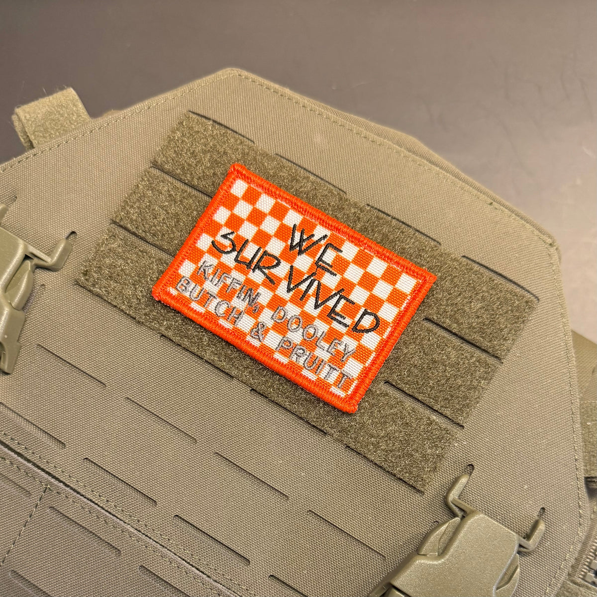 We Survived, Tennessee Football embroidered morale patch: tactical patch with an orange border and a white-and-orange checkered top, reading 'WE SURVIVED KAREN DOOLEY' in black script, shown attached to tan webbing on a matching.
