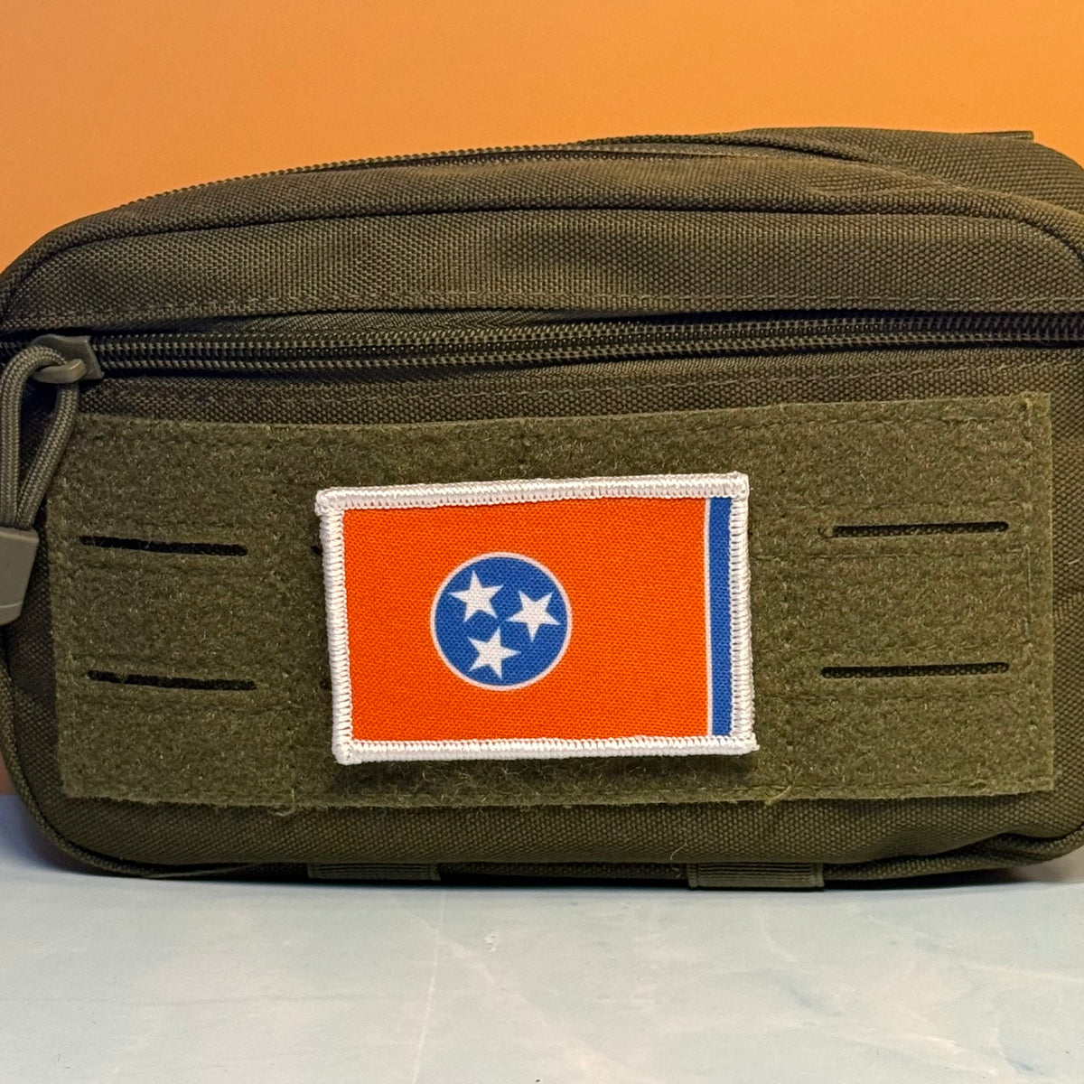 Tennessee Orange and Summitt Blue Flag printed canvas morale patch, an olive green tactical pouch featuring a rectangular Tennessee state flag patch on the front, set against a solid orange background.