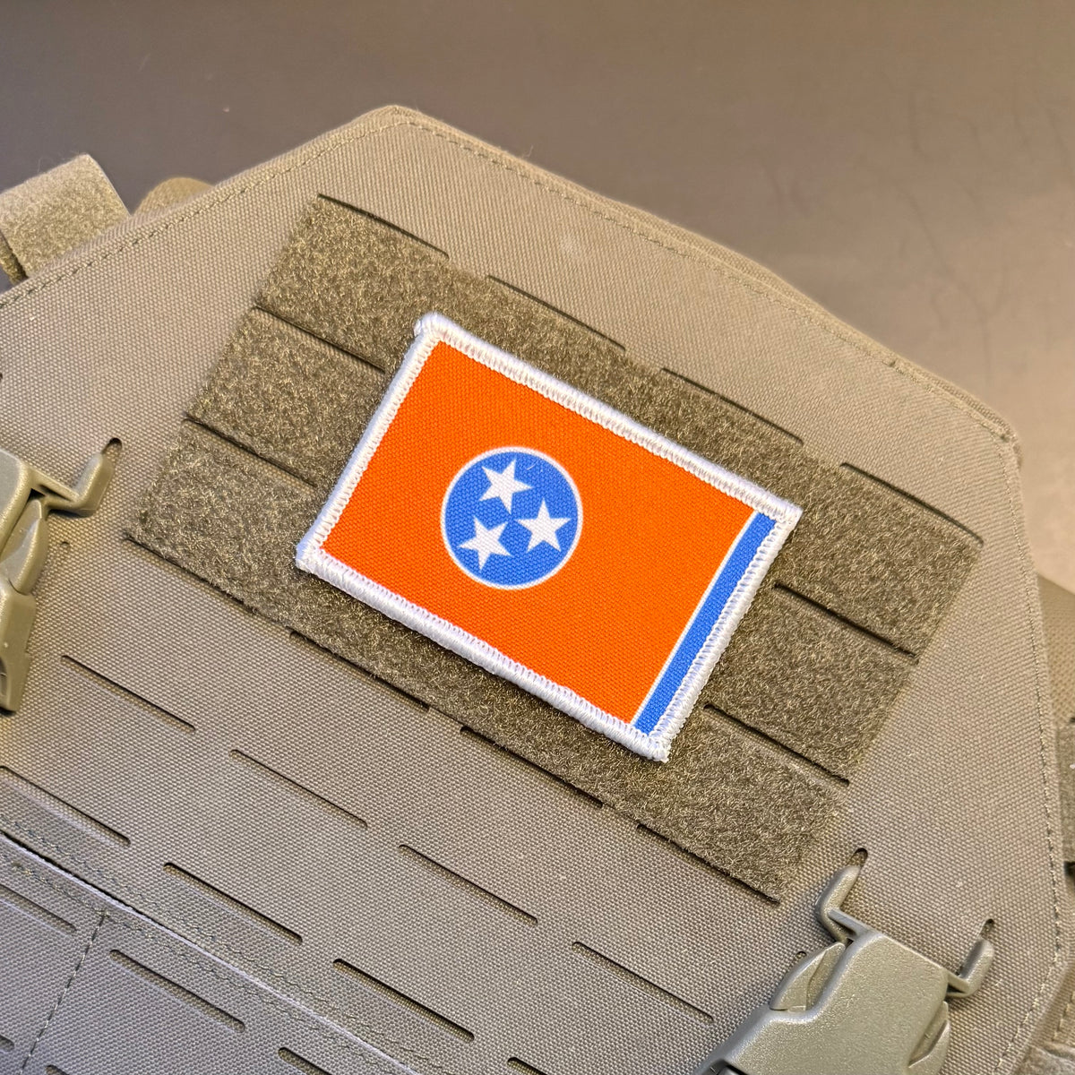 Tennessee Orange and Summitt Blue Flag printed canvas morale patch, an printed Tennessee state flag patch with an orange field, blue circle, and three white stars, shown attached to tan tactical gear with hook-and-loop fastening.