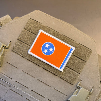 Tennessee Orange and Summitt Blue Flag printed canvas morale patch, an printed Tennessee state flag patch with an orange field, blue circle, and three white stars, shown attached to tan tactical gear with hook-and-loop fastening.