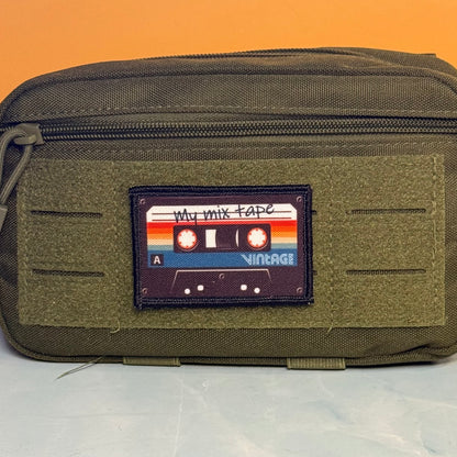 An olive green tactical pouch featuring a rectangular front patch designed to look like a vintage cassette tape with the text 'My mix tape' and 'VINTAGE'.