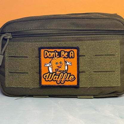 An olive green tactical pouch with a front hook-and-loop patch that reads 'Don't Be A Fun Waffle' with a cartoon waffle character, set against an orange background.
