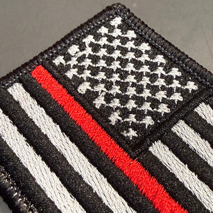 Thin Red Line American Flag Firefighter embroidered morale patch: featuring a black-and-white American flag design with a single red stripe running vertically, photographed on a dark gray surface.