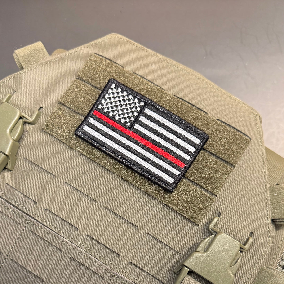 Thin Red Line American Flag Firefighter embroidered morale patch: black, white, and red 'Thin Red Line' American flag embroidered patch mounted on a tan tactical vest with velcro and quick-release buckles.