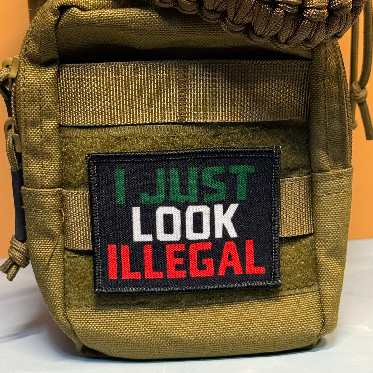 I Just Look Illegal printed canvas morale patch, a tactical pouch in olive drab green nylon with a black printed patch that the design lettering in green, white, and red lettering.