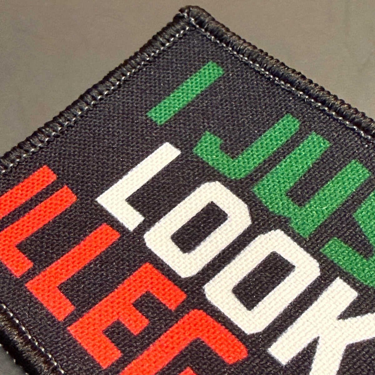I Just Look Illegal printed canvas morale patch, a close-up of a square printed patch with the design lettering in bold block letters. The patch has a black background with green, white, and red lettering, finished with a.