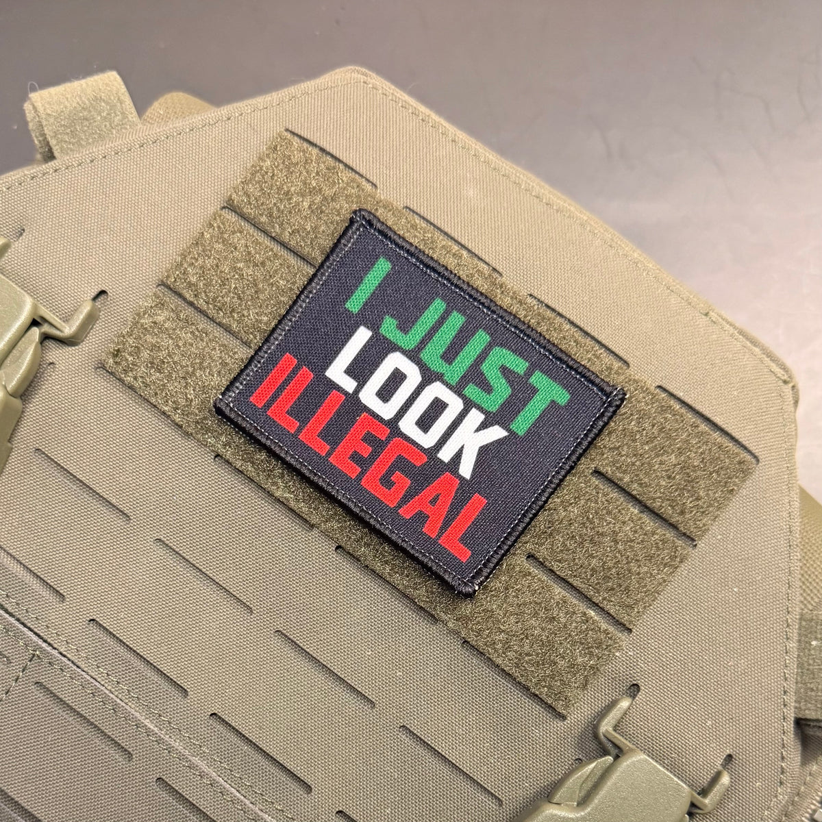 I Just Look Illegal printed canvas morale patch with the design lettering in green, white, and red on a black background, attached to a tan MOLLE tactical vest.