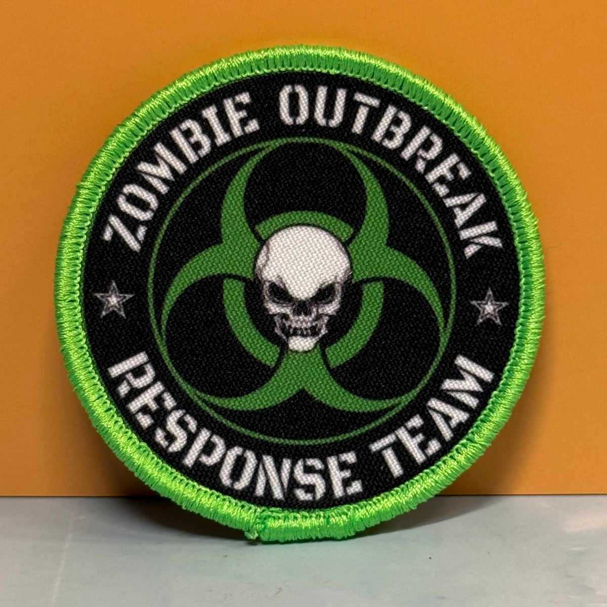 Zombie Outbreak Response Team printed canvas morale patch, black center, green biohazard symbol, white skull, and the design lettering on an orange background.