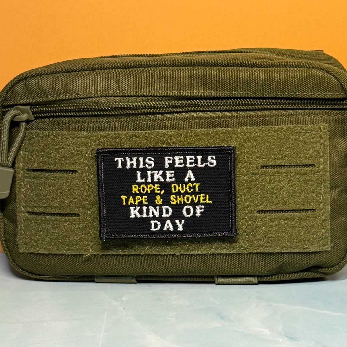 This Feels Like A Rope & Duct Tape Kind Of Day embroidered morale patch: olive green tactical pouch with a black rectangular patch that reads 'THIS FEELS LIKE A ROPE, DUCT TAPE & SHOVEL KIND OF DAY' in white and yellow text, set.