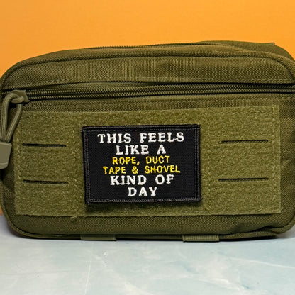 This Feels Like A Rope & Duct Tape Kind Of Day embroidered morale patch: olive green tactical pouch with a black rectangular patch that reads 'THIS FEELS LIKE A ROPE, DUCT TAPE & SHOVEL KIND OF DAY' in white and yellow text, set.