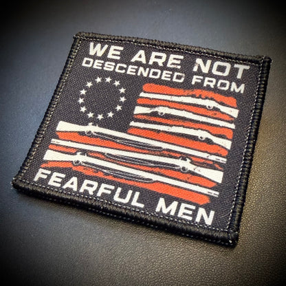A square embroidered patch with a black border and a stylized American flag design in black, white, and orange-red. The patch reads 'WE ARE NOT DESCENDED FROM' at the top and 'FEARFUL MEN' at the bottom, with a circle of stars on the upper left.